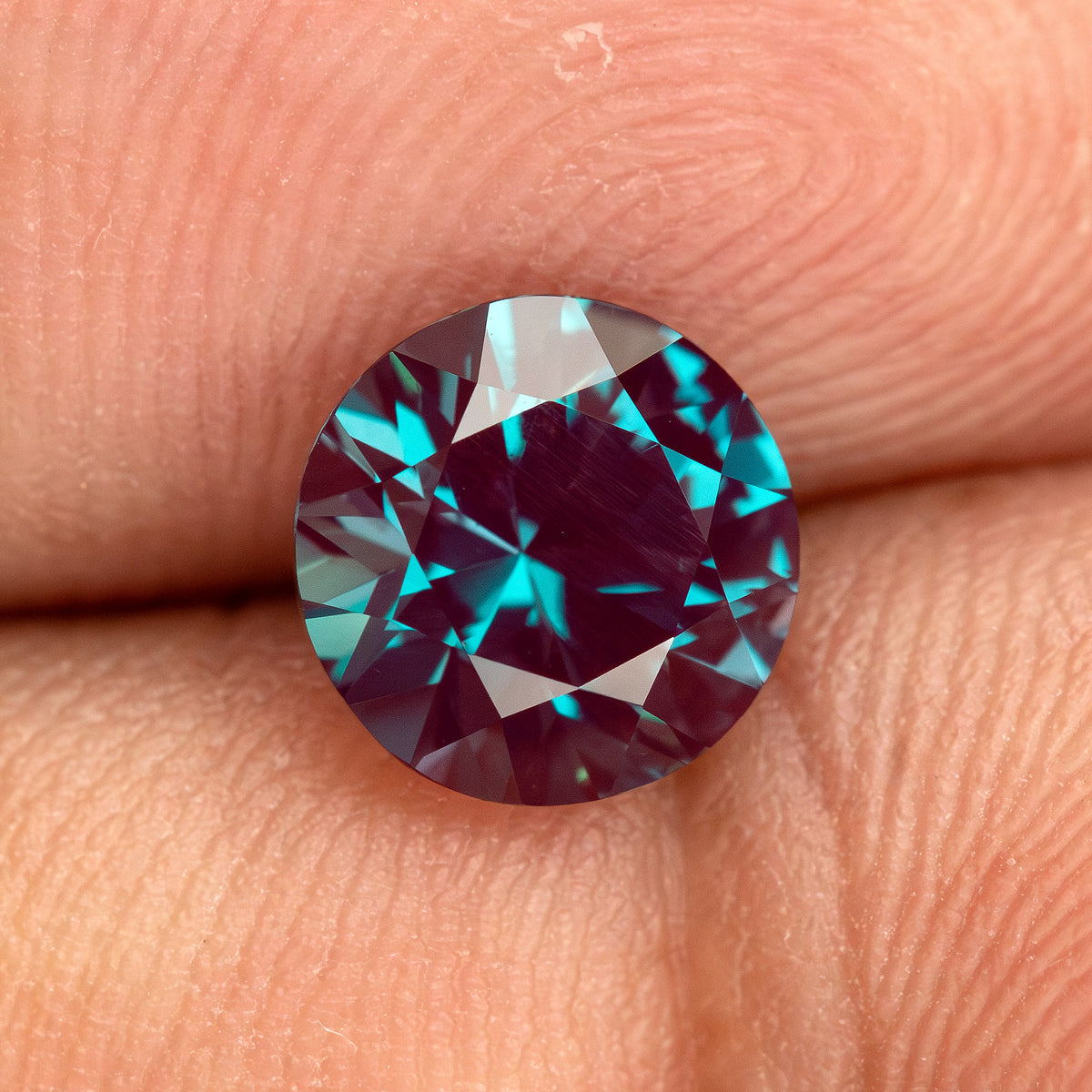 Crown-facing round sample on fingertips with blue-green and reddish reflections.