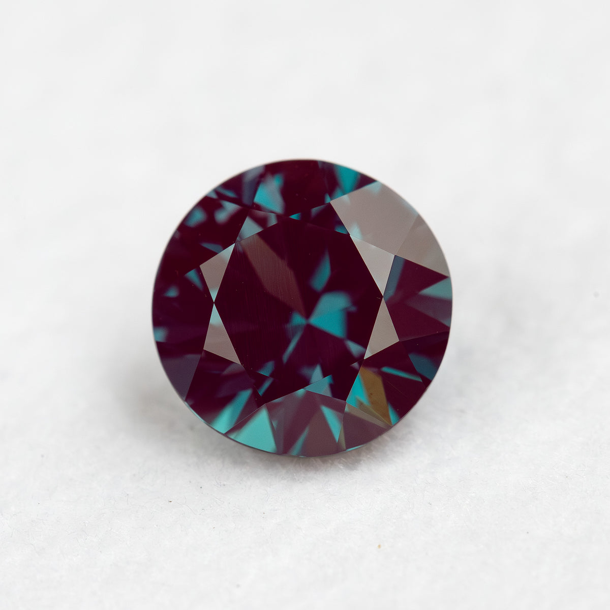 Face-up round lab-grown alexandrite sample on a pale surface, with its crown facets visible.