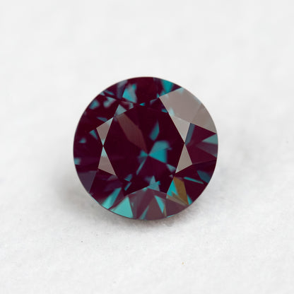 Face-up round lab-grown alexandrite sample on a pale surface, with its crown facets visible.