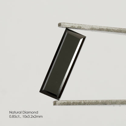 Reference black baguette diamond held diagonally in tweezers, with its complete rectangular outline and a bright reflection along one side.