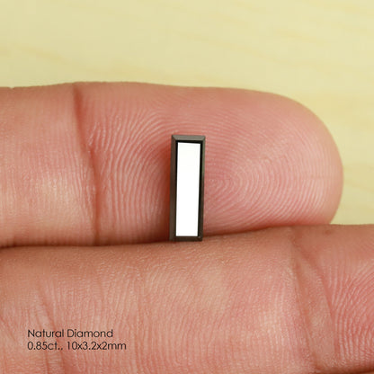 Reference black baguette diamond standing between fingertips for scale, with a broad white reflection across its table.