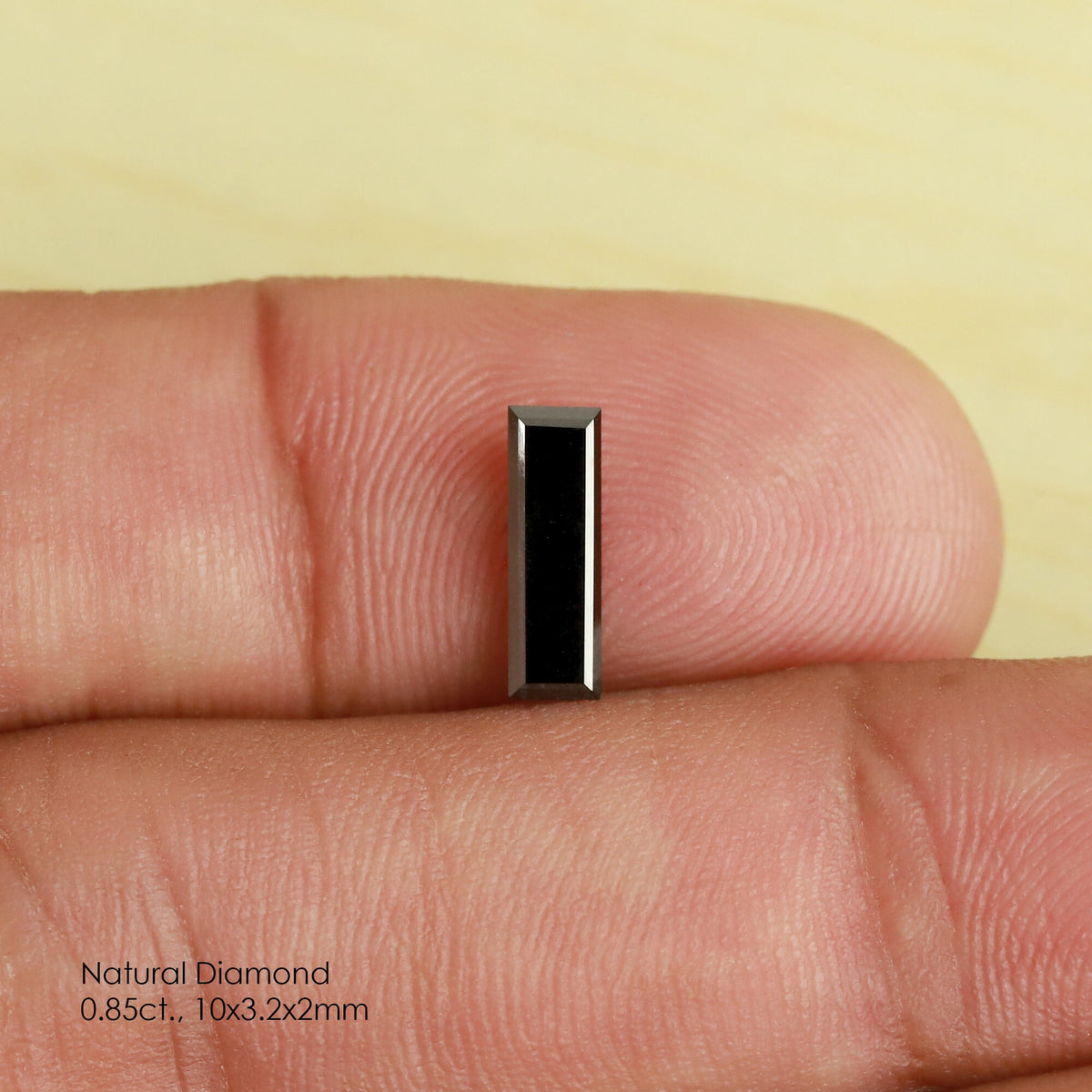 Reference black baguette diamond face-up between fingertips, showing its dark rectangular table and straight stepped edges.