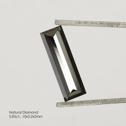 Reference black baguette diamond tilted in tweezers, with a bright lengthwise reflection across its central facet.