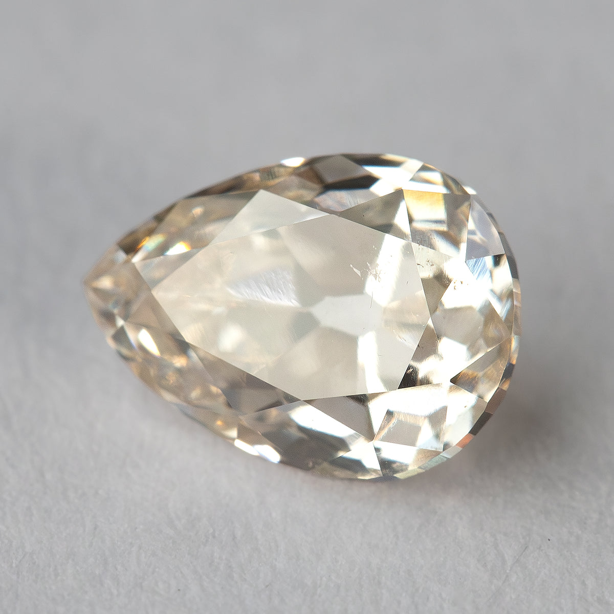 Angled face-up view of the loose pear-shaped diamond, showing warm reflections and its rounded shoulders.