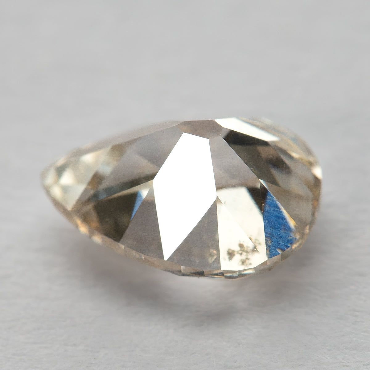 Pavilion-side view of the pear-cut diamond resting on a light surface, showing the back facets and inclusions.