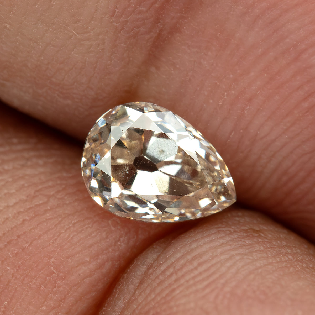 The light-champagne pear-cut diamond resting on a fingertip, providing a visual scale reference.