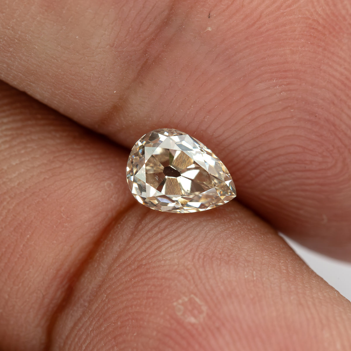 Wide hand-scale view of the loose pear diamond, showing its size and warm appearance against a fingertip.