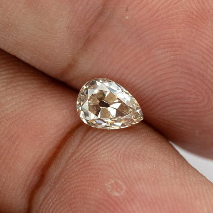 Wide hand-scale view of the loose pear diamond, showing its size and warm appearance against a fingertip.