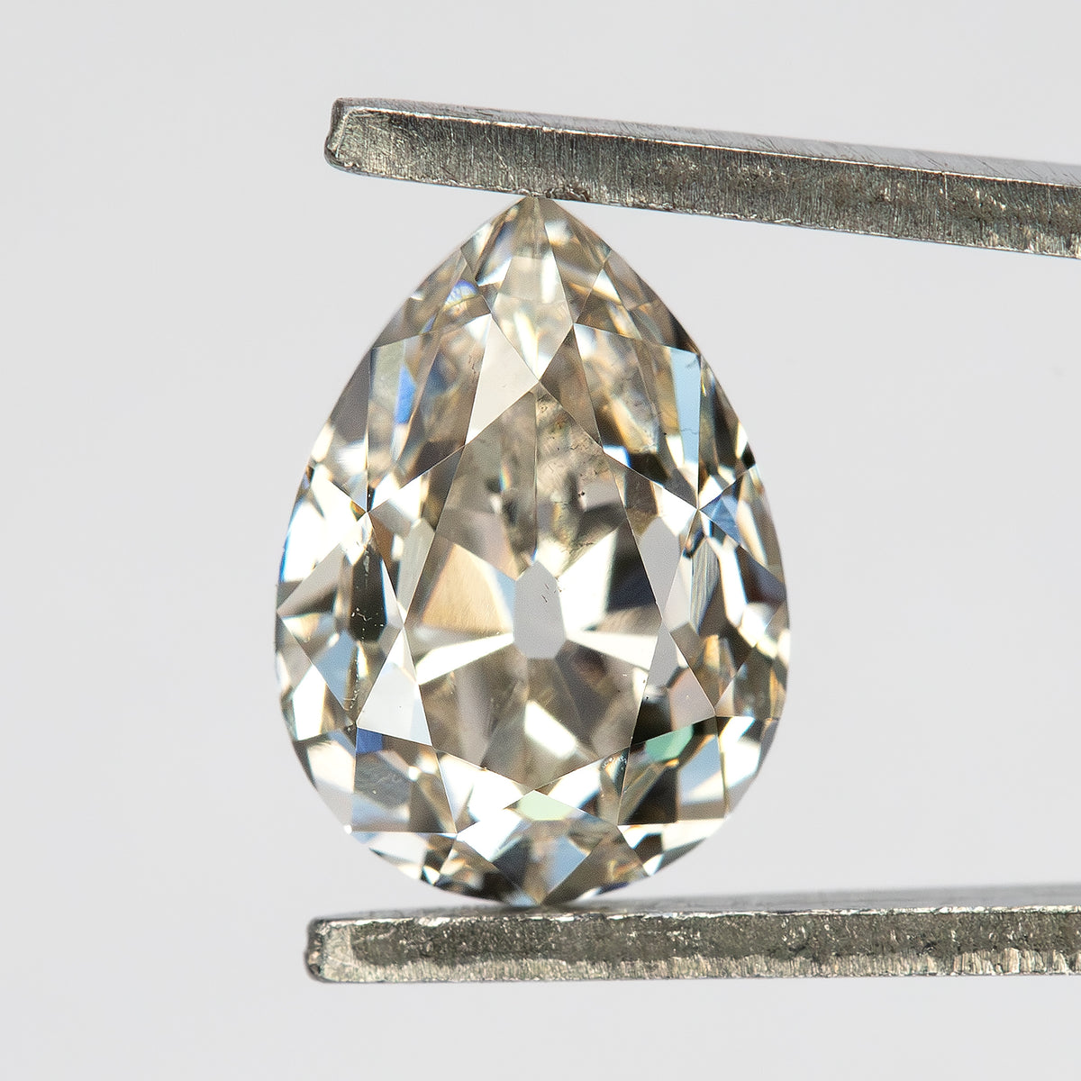 Face-up view of the light-champagne pear diamond held vertically in tweezers, showing the full outline.