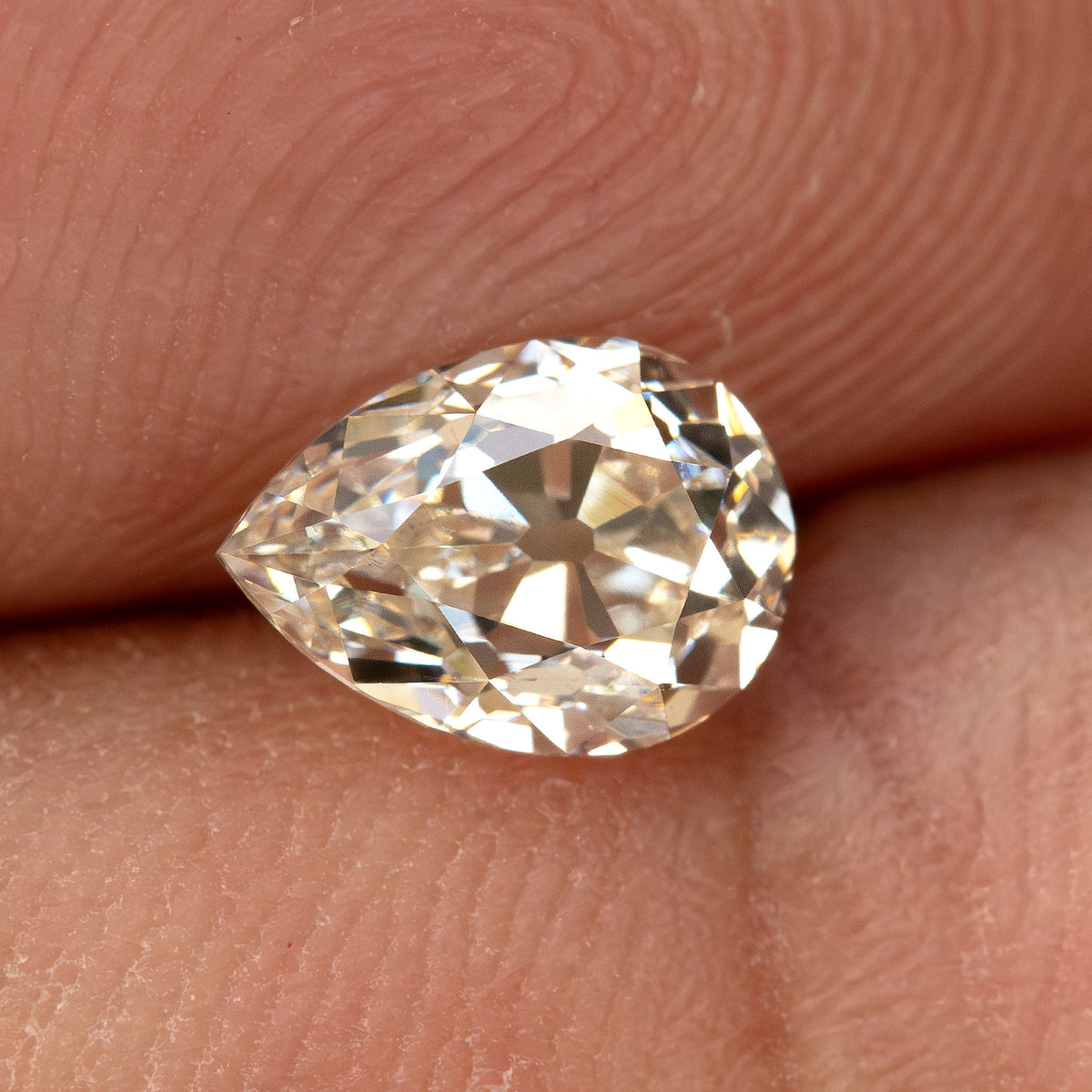 Wider hand-scale view of the exact light-champagne pear diamond against a fingertip.