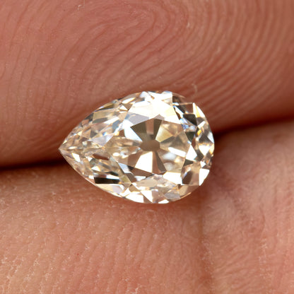 Wider hand-scale view of the exact light-champagne pear diamond against a fingertip.