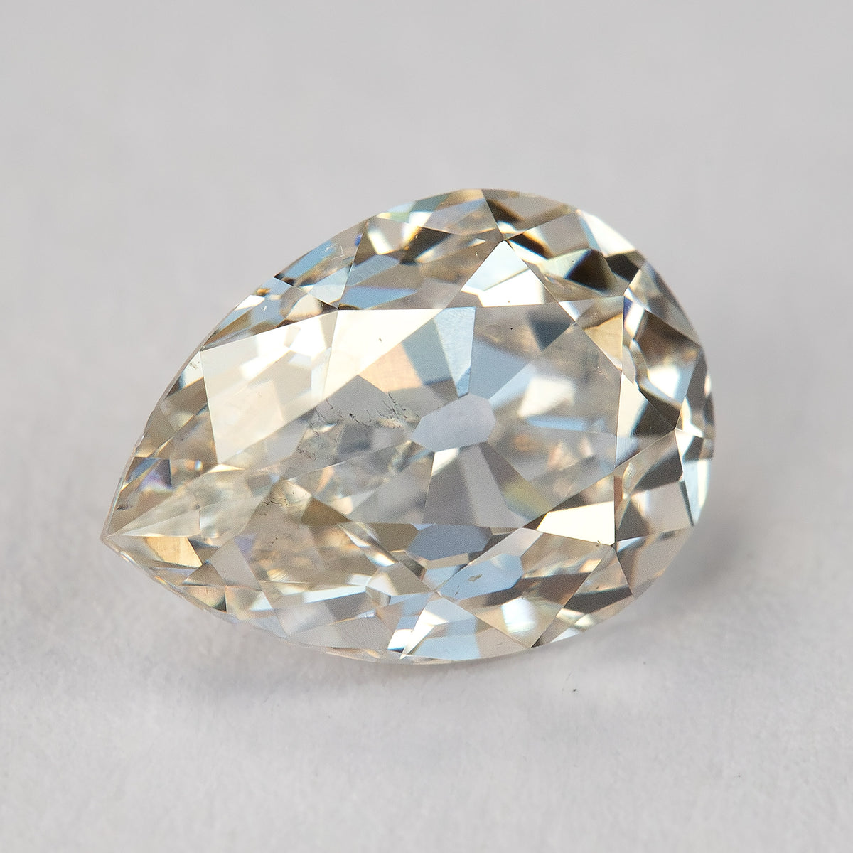 Face-up view of the exact light-champagne old-mine pear-cut diamond on a light surface, showing its outline, broad facets and visible characteristics.
