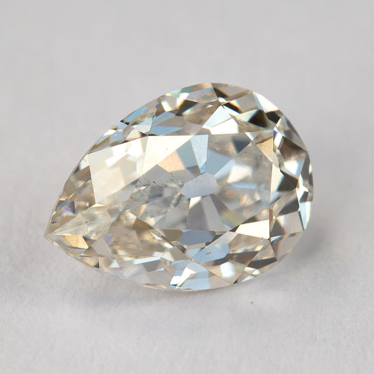 Face-up view of the exact light-champagne old-mine pear-cut diamond on a light surface, showing its outline, broad facets and visible characteristics.