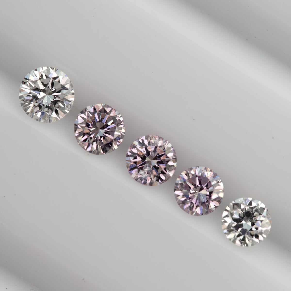 Diagonal row of purplish-pink round diamond samples between two white comparison diamonds; white references are not included.