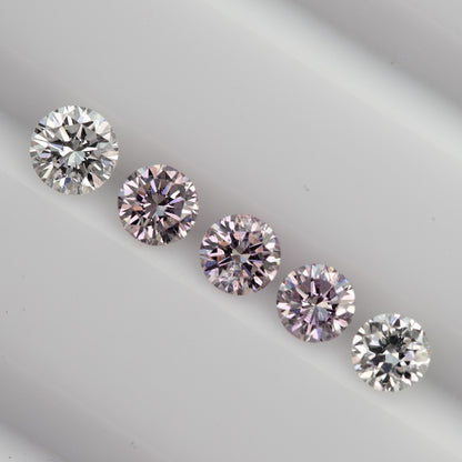 Diagonal row of purplish-pink round diamond samples between two white comparison diamonds; white references are not included.
