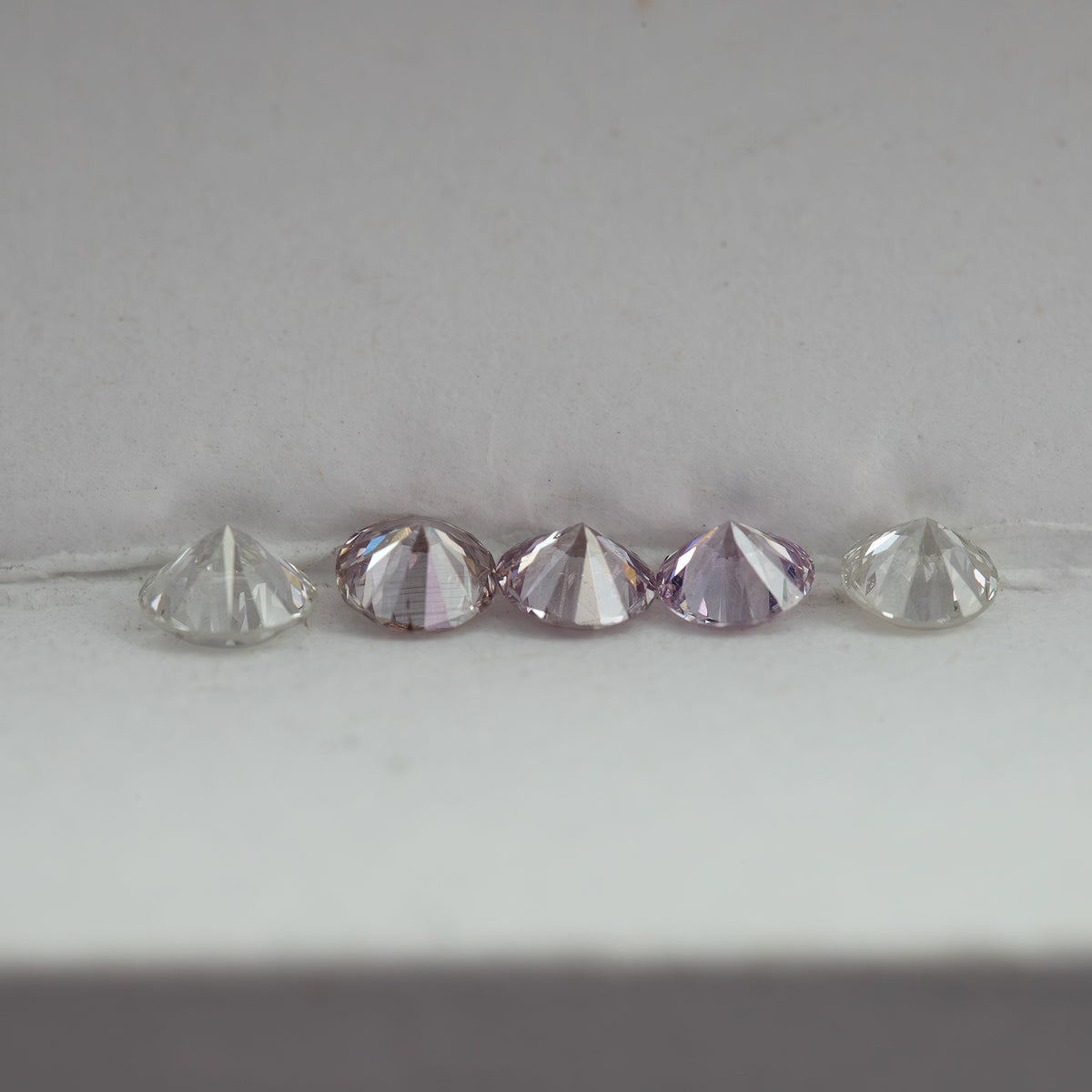 Low side-profile view of pink round diamond samples between white comparison stones, showing crown and pavilion depth.