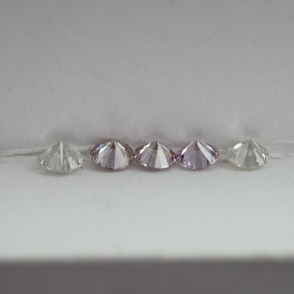 Low side-profile view of pink round diamond samples between white comparison stones, showing crown and pavilion depth.