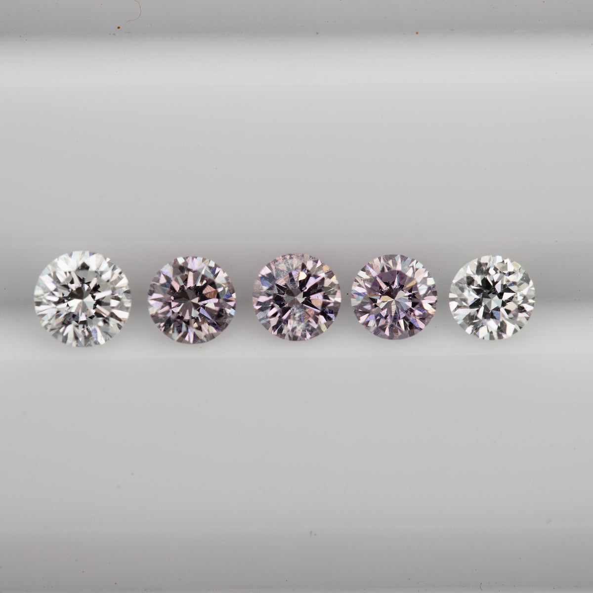 Horizontal face-up row of pink round diamond samples with white color-reference diamonds at both ends.