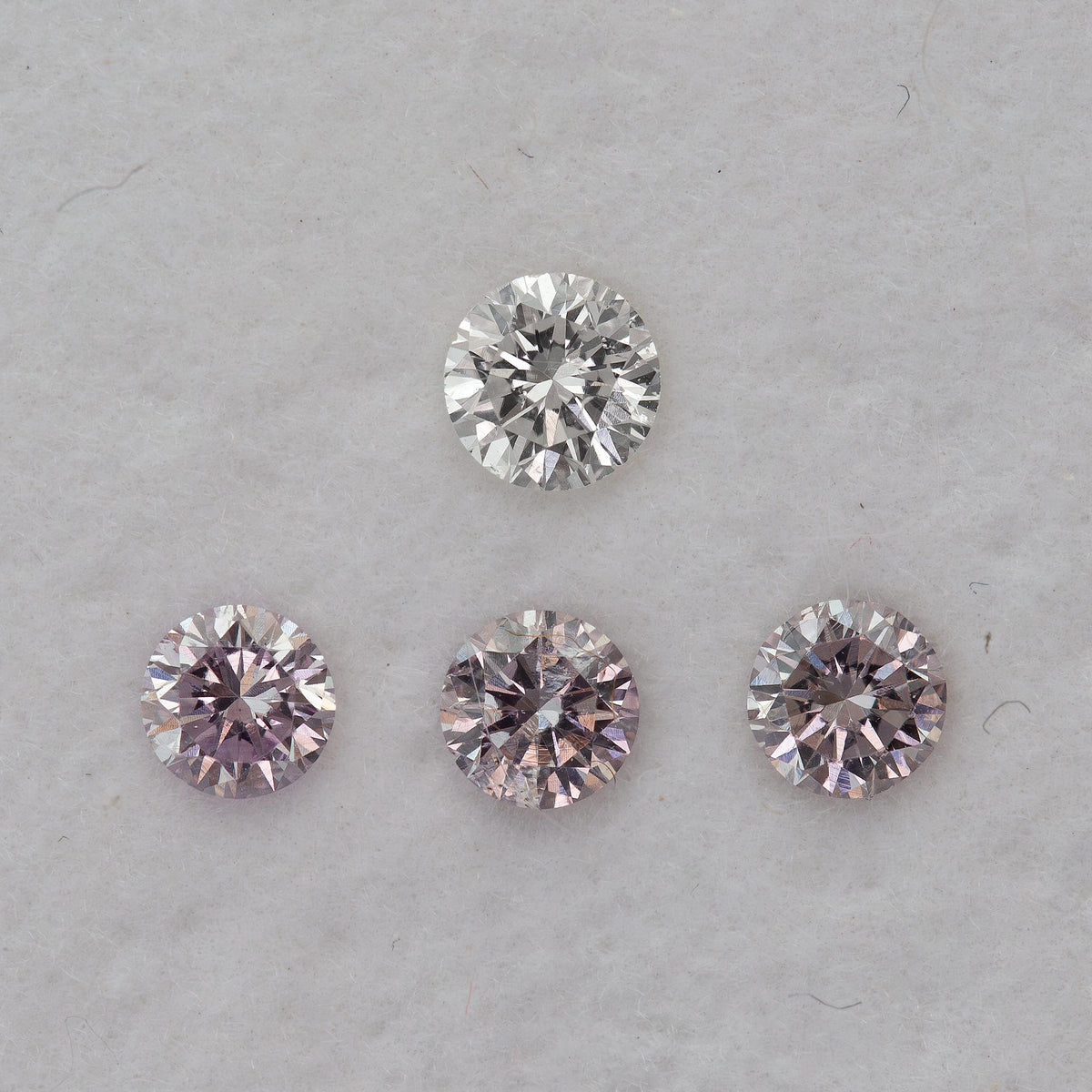 Face-up pink round diamond samples beneath one white comparison diamond on a pale background; purchase is per pink diamond.