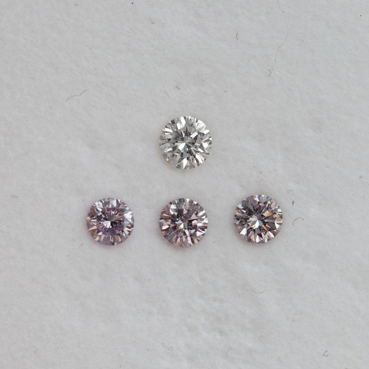 Spaced face-up group of purplish-pink round diamond samples below a white comparison stone, showing reflected color.