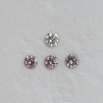 Spaced face-up group of purplish-pink round diamond samples below a white comparison stone, showing reflected color.