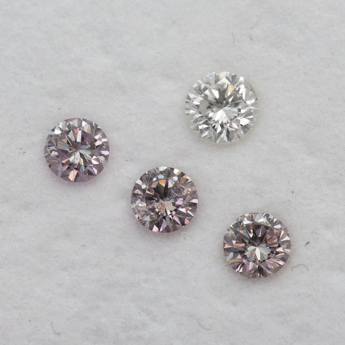 Diagonal face-up arrangement of pink round diamond samples beside one white color-reference diamond.