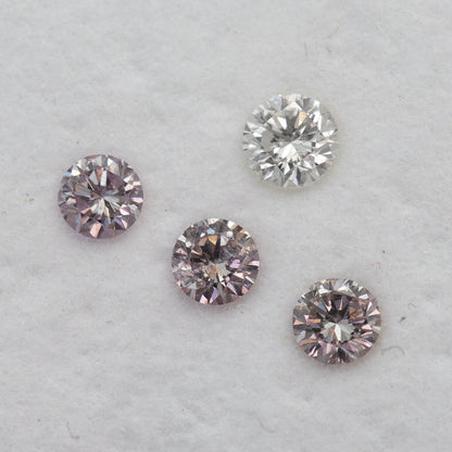Diagonal face-up arrangement of pink round diamond samples beside one white color-reference diamond.