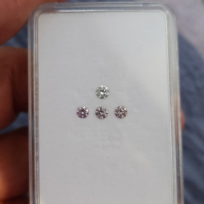 Hand holding an open gem box with pink round diamond samples and a white comparison stone, providing scale context.