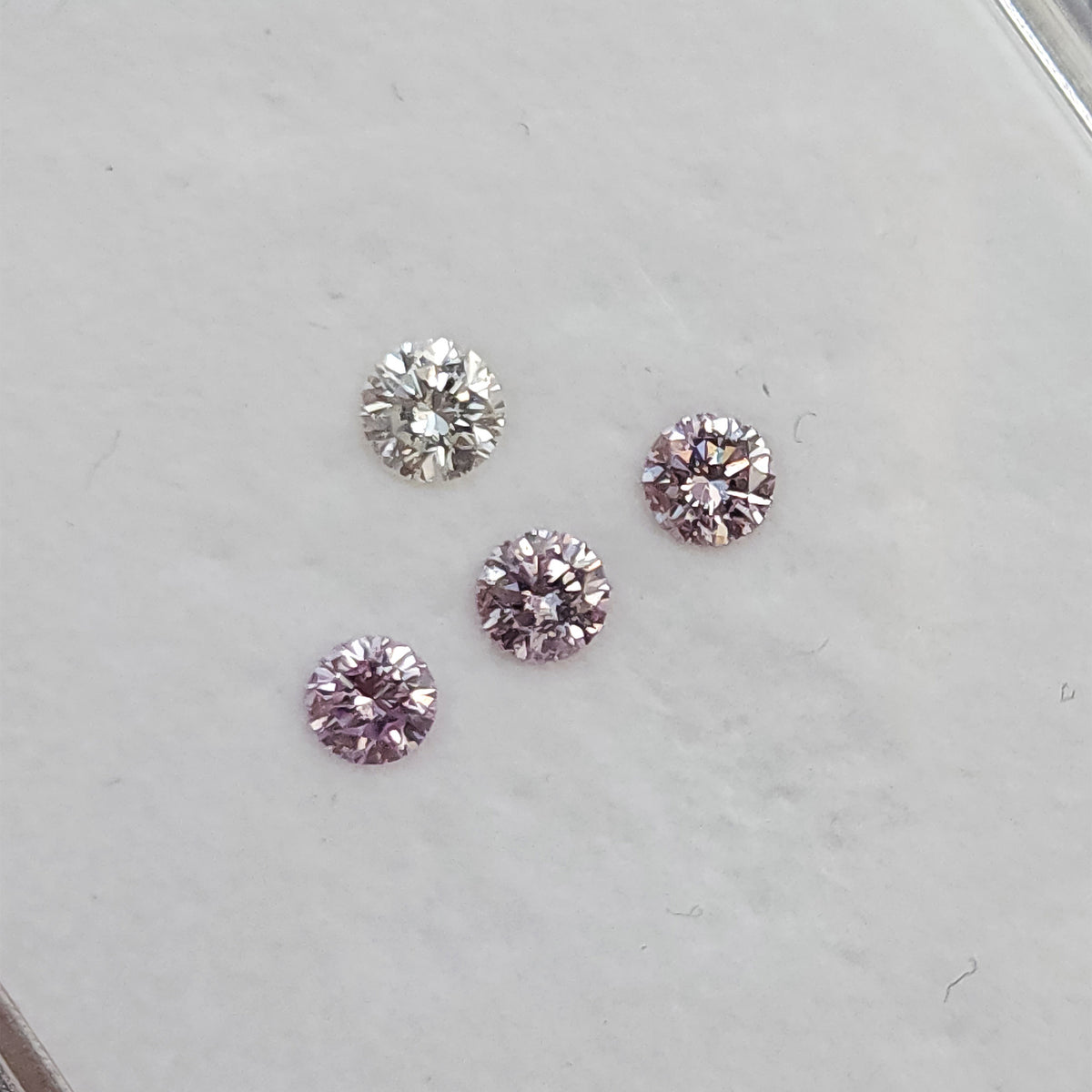 Angled group of pink round diamond samples with a white comparison stone on the pale gem-box surface.
