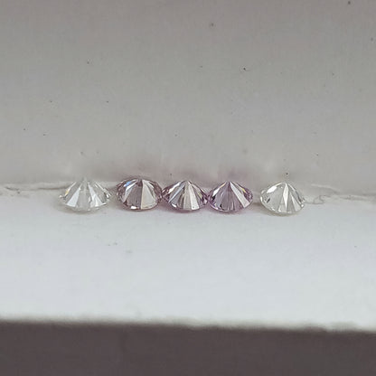 Close low-profile row of pink round diamond samples and white comparison stones, showing the pointed pavilion shapes.