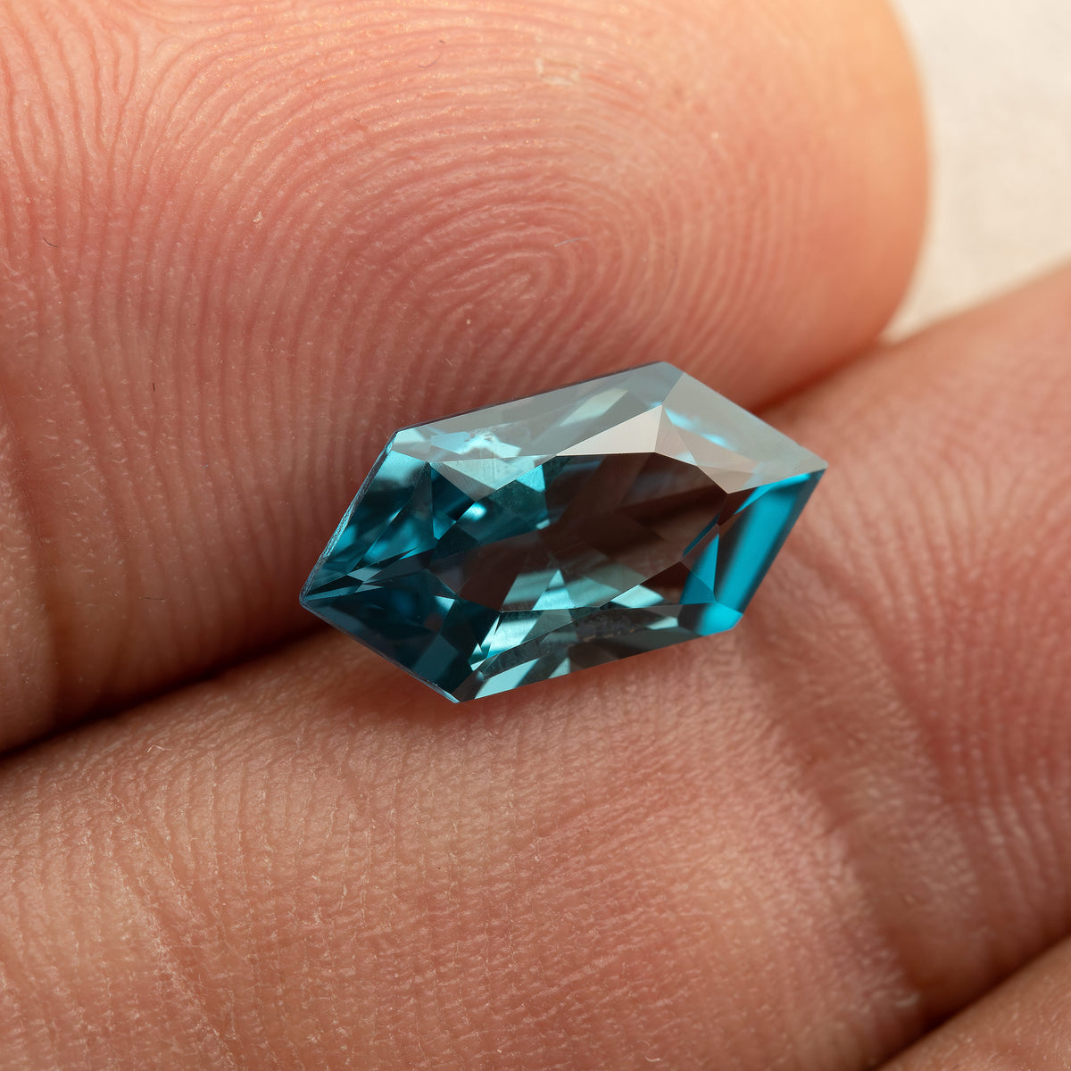 Wider view of a teal lab-grown sapphire against fingers for scale.