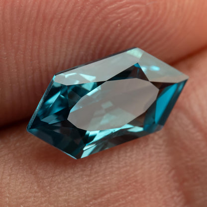 Angled close-up of a teal lab-grown sapphire against fingers, showing a broad pale central reflection.