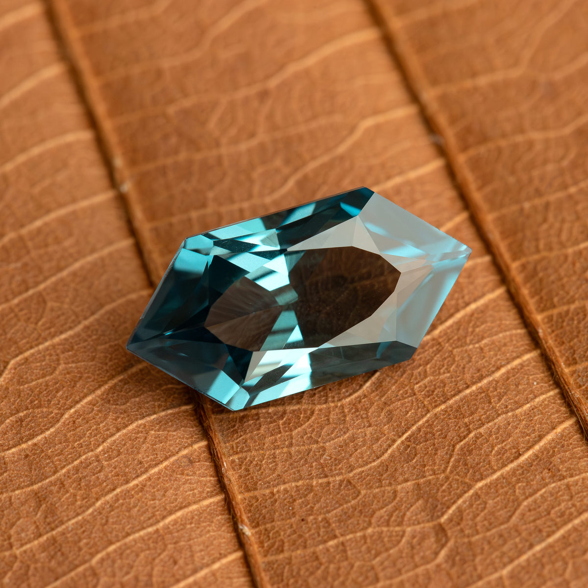 Wider view of a teal lab-grown sapphire on a brown leaf, showing its size relative to the leaf veins.