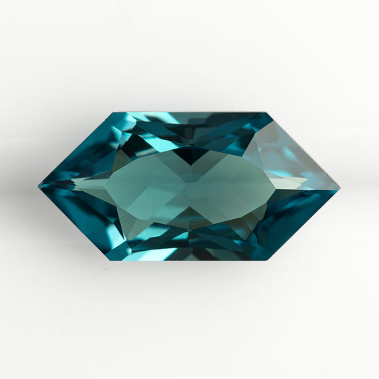 Face-up view of a teal green-blue lab-grown sapphire on a white background, showing its elongated hexagonal shape.