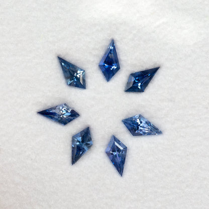 Seven blue kite-shaped sapphires arranged in a circle on a white pad, seen from above.