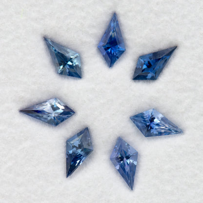 Overhead close-up of seven blue kite-shaped sapphires, showing their different outlines and blue tones.