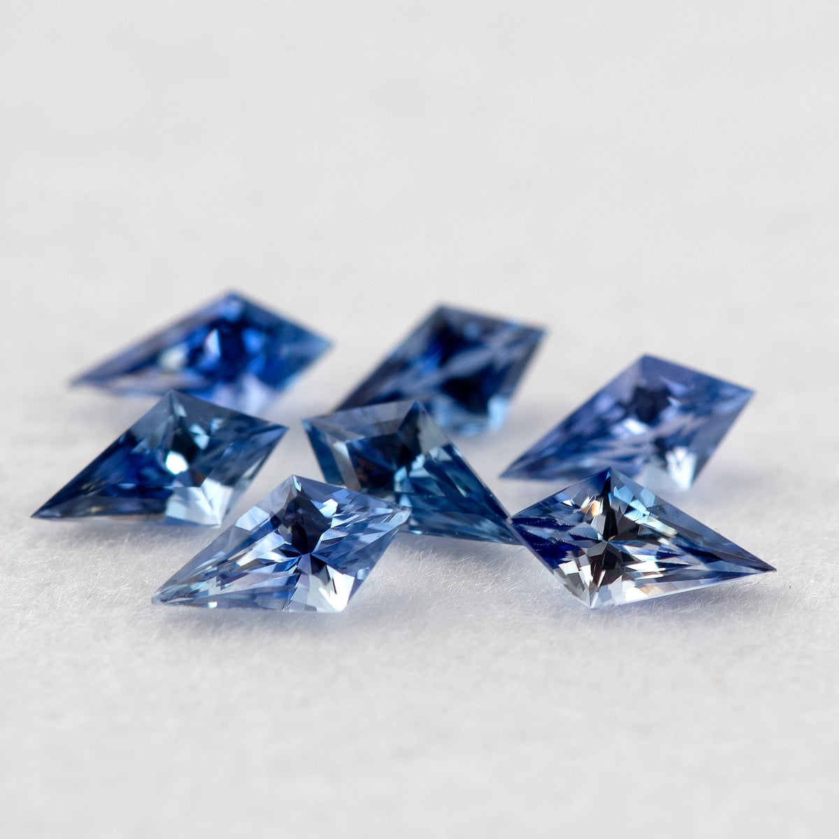 Low angled view of seven blue kite-shaped sapphires, showing their raised profiles above the white surface.