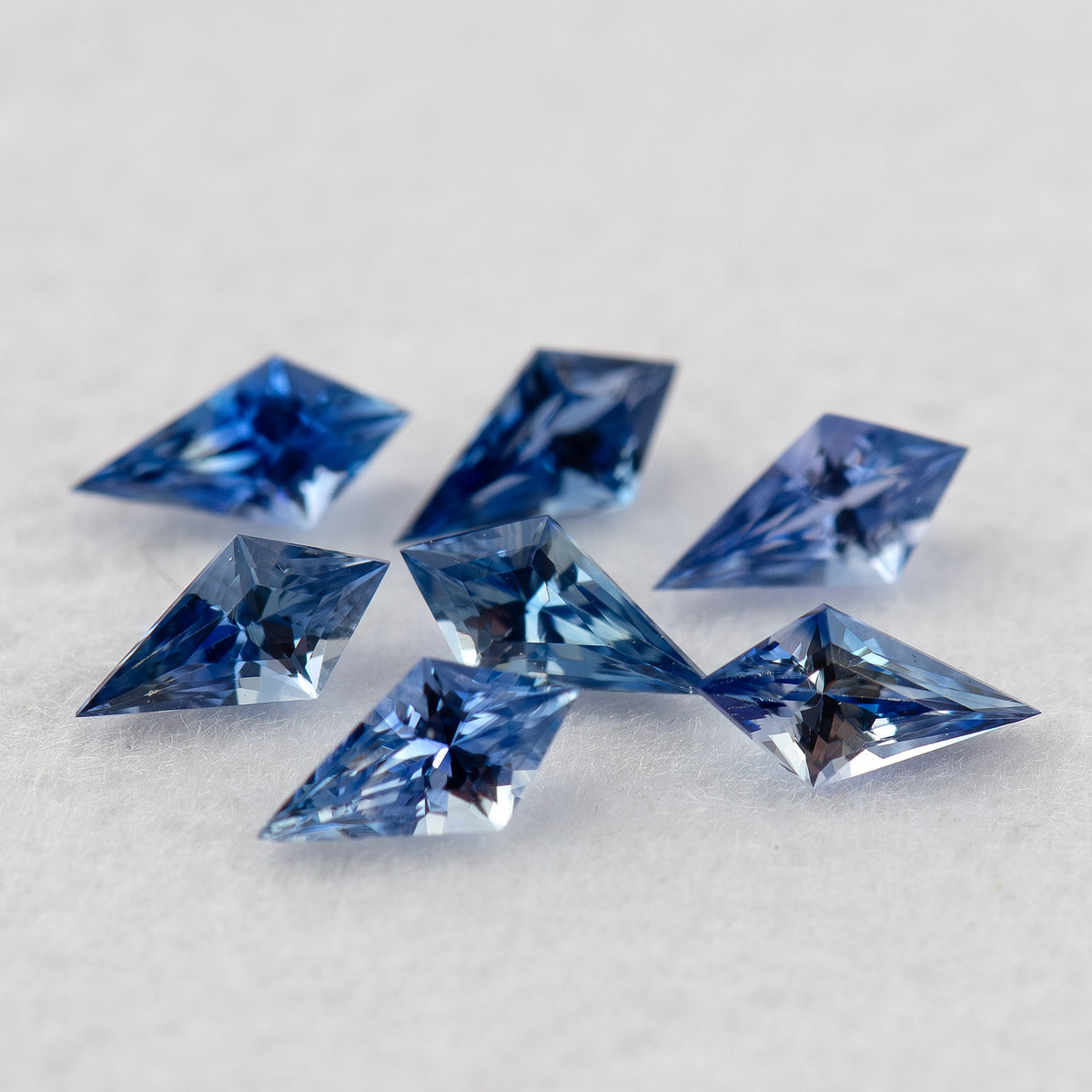 Close angled view of the seven loose blue sapphires, with brighter front stones and softer background stones.