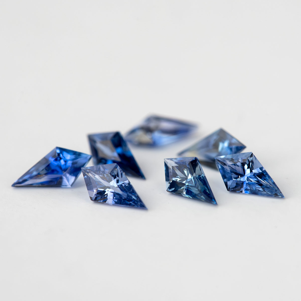 Low profile view across the blue sapphire parcel, emphasizing the stones raised above the white background.