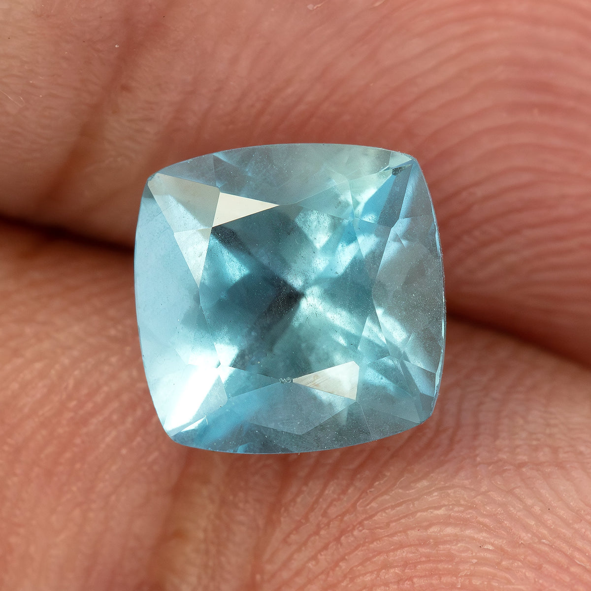 Acuamarina exacta de 2.08 ct descansando sobre la yema de un dedo para escala, con inclusiones visibles y reflejos frontales brillantes.