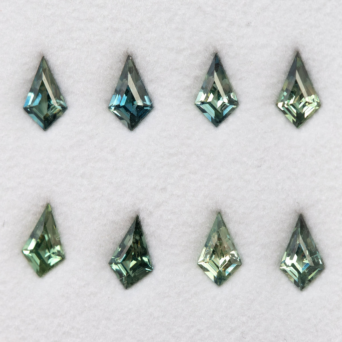 Original group of eight green and teal kite-shaped sapphires arranged in two rows on a pale surface.
