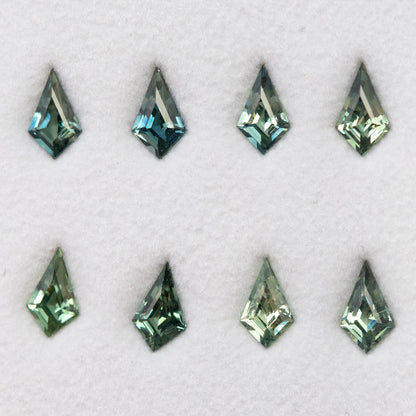 Original group of eight green and teal kite-shaped sapphires arranged in two rows on a pale surface.