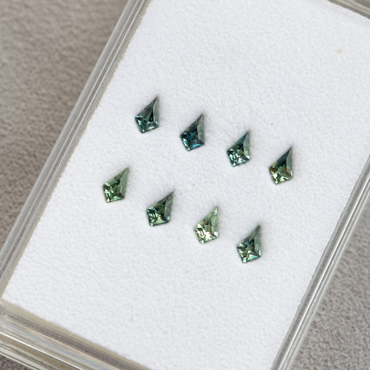 Eight small kite sapphires in a clear gem tray, viewed diagonally.
