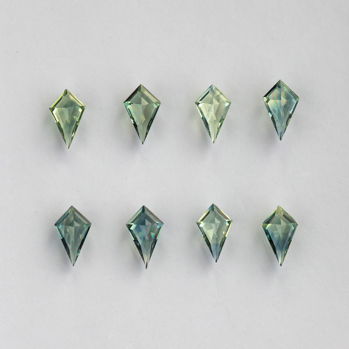 Pavilion-side view of the original eight kite sapphires on a pale surface.