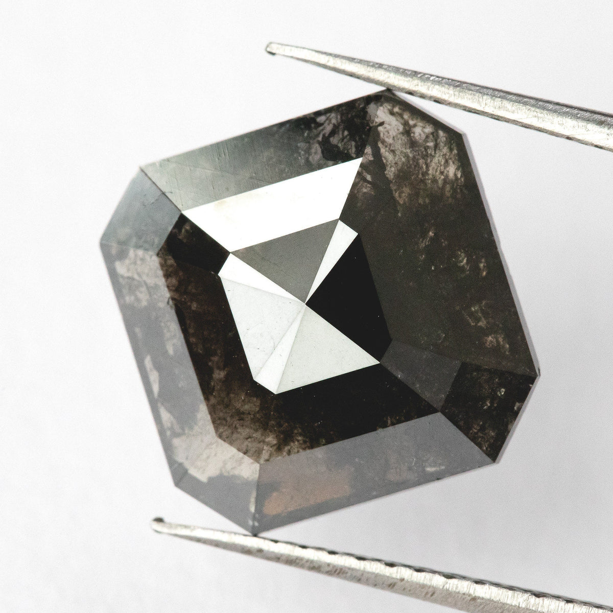 Brownish-black natural diamond held face-up in tweezers, showing the clipped-square outline, broad triangular facets and visible internal markings.