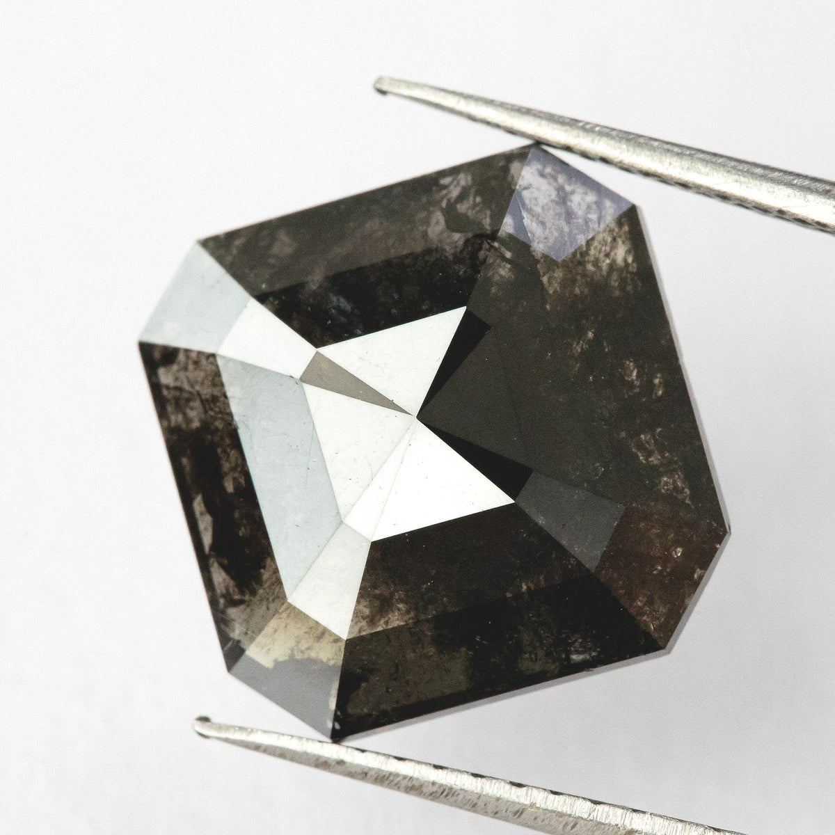 Brownish-black rose-cut diamond tilted slightly in tweezers, with a bright triangular reflection across the crown.