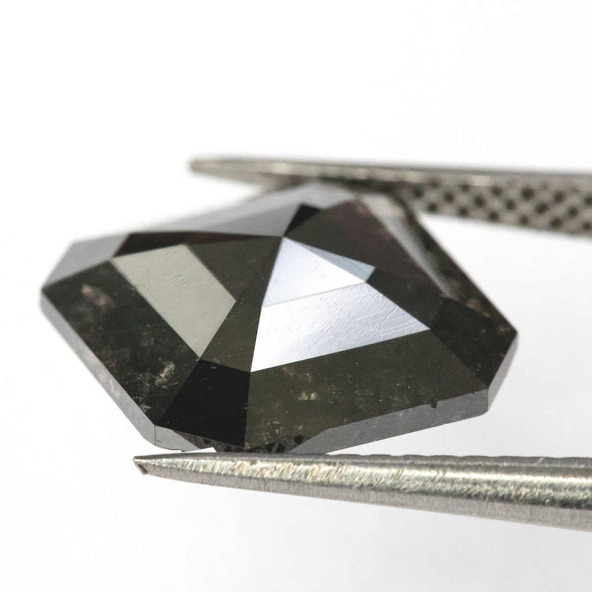 Low oblique view of the brownish-black diamond in tweezers, showing the raised rose-cut crown and broad geometric facets.