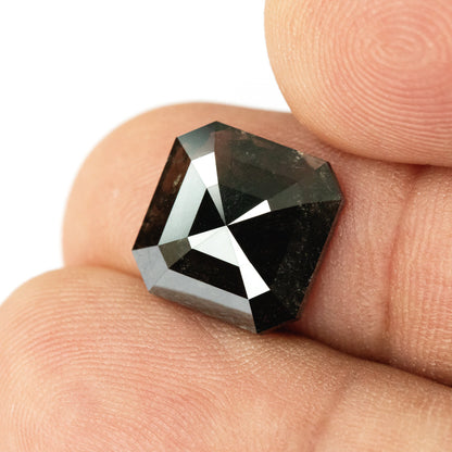 Brownish-black diamond resting face-up against fingertips, giving real-life scale and showing bright triangular facet reflections.