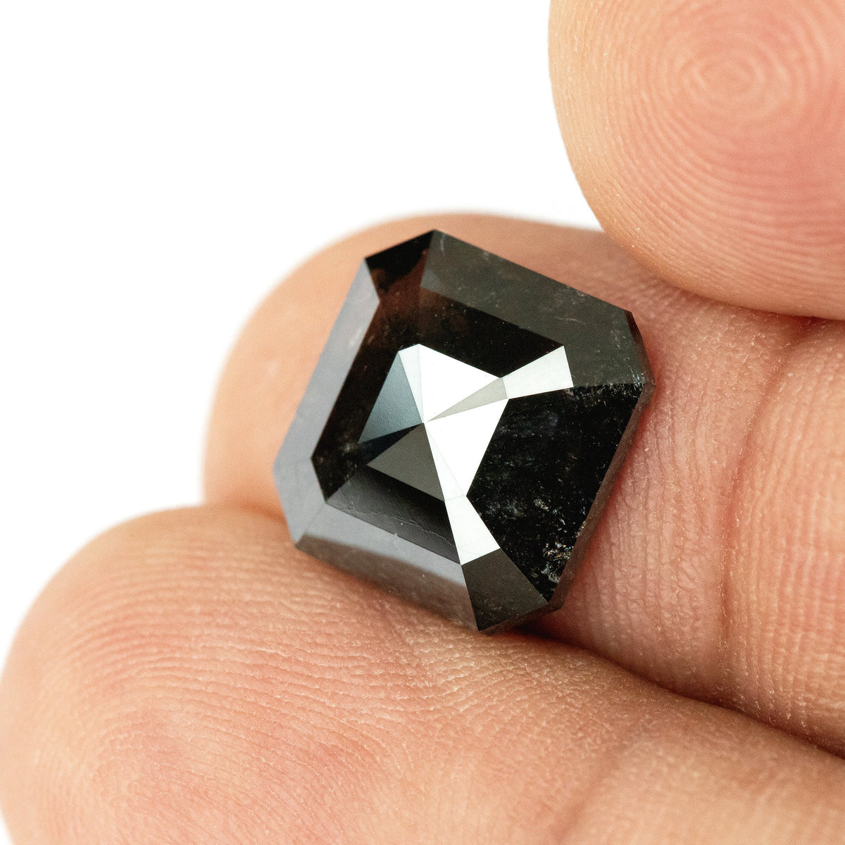 Brownish-black rose-cut diamond held against a fingertip at a slight tilt, showing contrasting dark and bright crown facets.