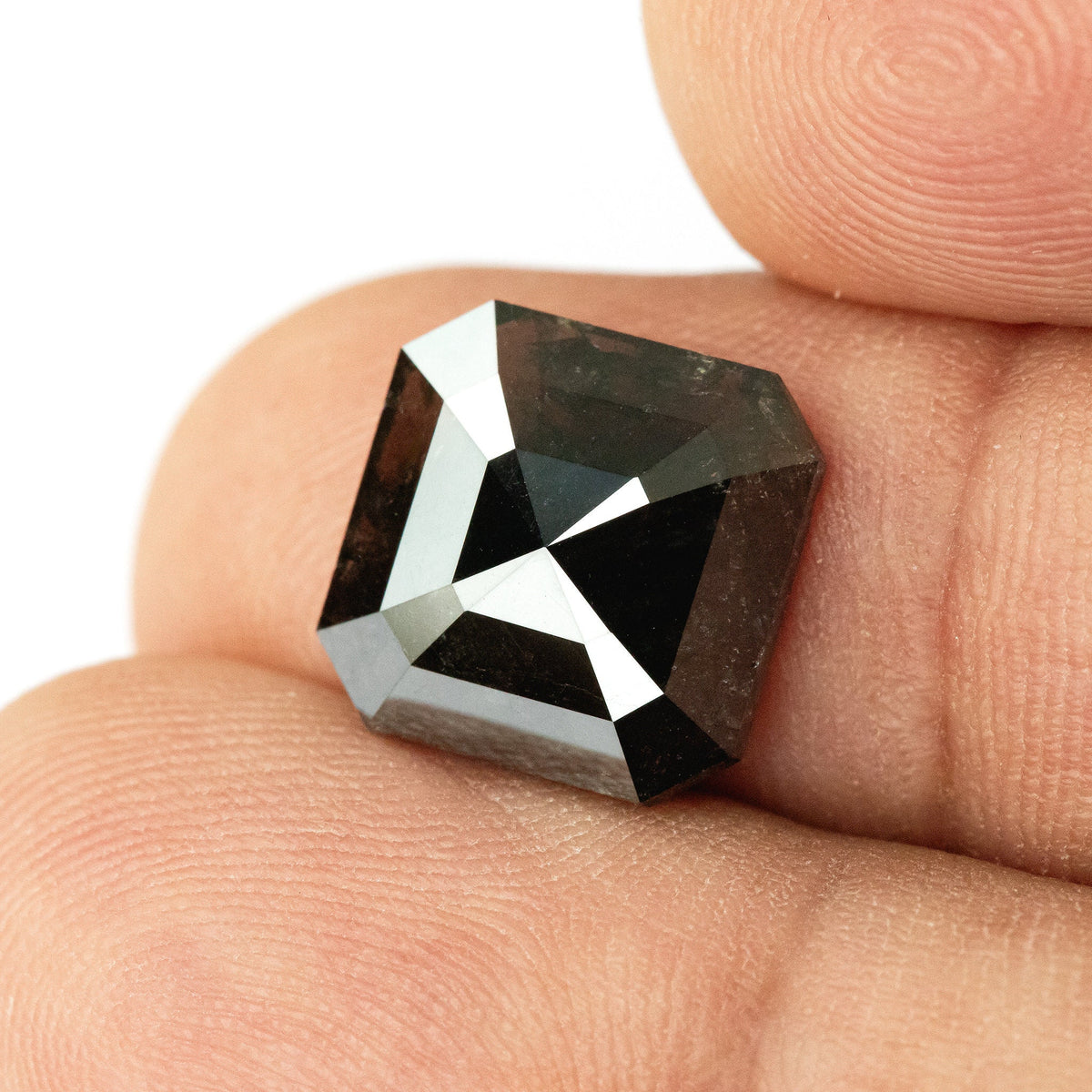 Clipped-square brownish-black diamond against fingertips, with the complete outline and broad crown facets visible.